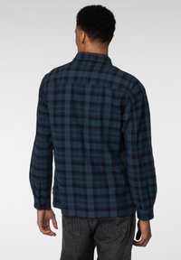 Blå og svart rutete skjorte laget av tykt stoff, med lange ermer, knappefester og klassisk krage. Detaljert bakyoke-design.