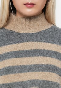 Grå og beige stripete høyhalset genser laget av mykt strikkemateriale, med ribbet krage og varierende bredder på stripene for tekstur.