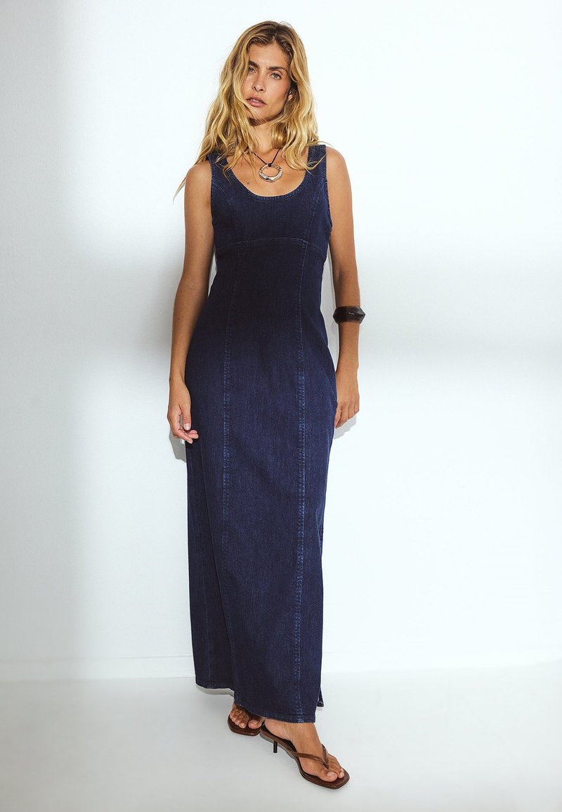 Tume sinine teksamaksikleit, millel on ümmardatud kaelus, voodi ja A-lõige. Omab minimaalset õmblemist ja kontrastsete värvide aktsente.