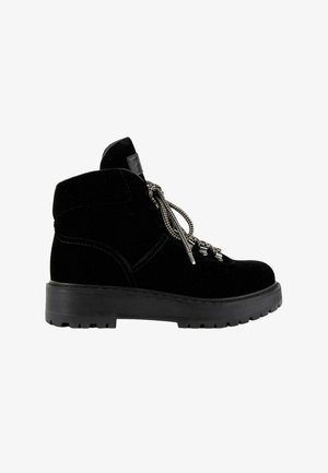 Bota de ante negro hasta el tobillo con suela gruesa de goma, puntera redonda, ojales metálicos y cordones con estampado en blanco y negro.