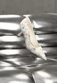 Chaussure à talon haut florale avec un bout pointu, en matériau texturé crème, motif de fleurs pastel, et un petit talon bloc.