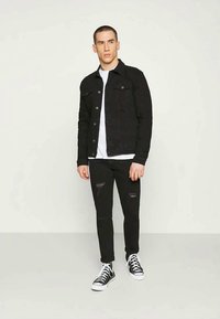 Svart denimjacka med två bröstfickor, bärs över en vit t-shirt. Svarta ripped jeans och svarta högklackade sneakers fulländar outfiten.
