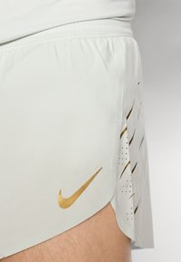 Shorts deportivos de color gris claro con un logo dorado de Nike, una cintura texturizada y detalles perforados a lo largo del costado para mayor transpirabilidad.