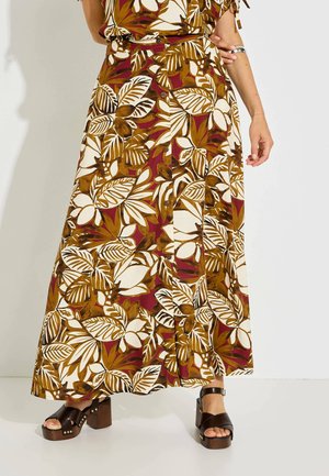 Mujer con una falda larga con estampado floral con hojas marrones, blancas y burdeos, combinada con sandalias de plataforma marrón oscuro.