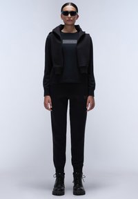 Zwarte casual outfit met een hoodie en bijpassende sweatpants, gemaakt van zachte stof. Stevige zwarte laarzen maken de look compleet.