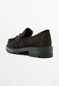 Mocassini in suede marrone scuro con finitura texturizzata, suola in gomma verde spessa e dettagli decorativi a frange sulla parte anteriore.