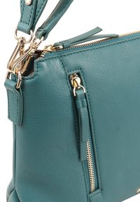 Teal leren handtas met een gestructureerde afwerking, voorzien van gouden hardware, dubbele ritsen en een afneembare strap voor veelzijdige draagmogelijkheden.