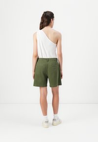 Top branco de um ombro só combinado com calções verdes, apresentando uma cintura elástica, dois bolsos traseiros e um corte solto. Ténis completam o look.