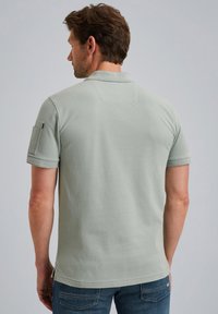 Světle zelené polo tričko s krátkými rukávy, standartním límečkem a náprsní kapsou na levém rukávu. Bavlněný materiál, jemná textura.