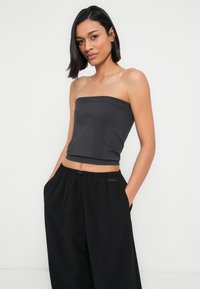 Haut noir sans bretelles avec texture côtelée et détail géométrique. Associé à un pantalon noir ample avec cordon de serrage et accents de logo.