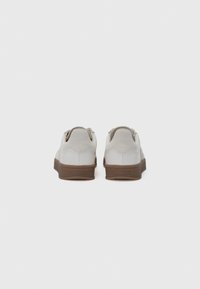 Baskets blanches avec une tige en cuir lisse et des accents en daim. Elles disposent d'une semelle en caoutchouc marron et d'un branding subtil sur le talon.
