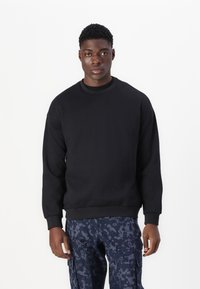 Svart sweatshirt med rundad halsringning och ribbad mudd, tillverkad av texturerad tyg. Bärs med mönstrade marinblå cargobyxor.