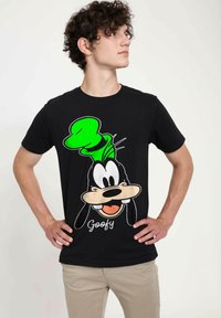 Černé tričko s potiskem kreslené postavičky v zelené čepici a velkým úsměvem. Pod postavičkou je vytištěný text "Goofy". Standardní střih.
