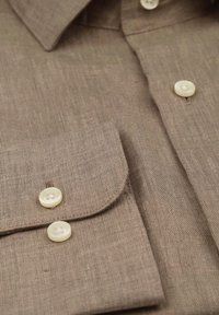 Bruine linnen shirt met een puntige kraag, flapzak en tan knopen. Geweven stof met een subtiel structuurpatroon.