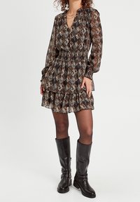 Robe à motifs marron avec des manches longues, un ourlet à volants et un col en V. Associée à des bottes en cuir noires arrivant au genou avec des accents de boucles.