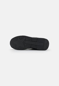 Black sneaker sole with textured pattern, featuring grooves and star-shaped design elements for traction. Durable rubber material.