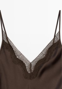 Hnědá saténová halenka s výstřihem do V, obohacená o jemné krajkové lemy a tenký třásněný okraj podél okrajů. Nastavitelné tenké ramínka.