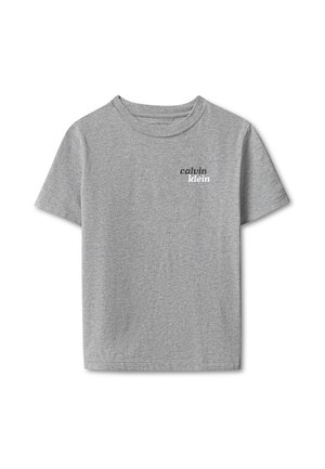 Kind draagt een grijs Calvin Klein T-shirt en donkergewassen jeans, staat met de rug naar de camera tegen een effen grijze achtergrond.