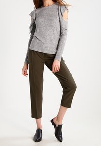 Maglietta grigia a maniche lunghe con dettagli a volantino sulle spalle, abbinata a pantaloni cropped verde oliva e scarpe nere slip-on.