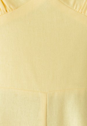 Close-up van een lichtgele, textuurrijke stof met een naad en gegatherde stikdetails aan de bovenkant.