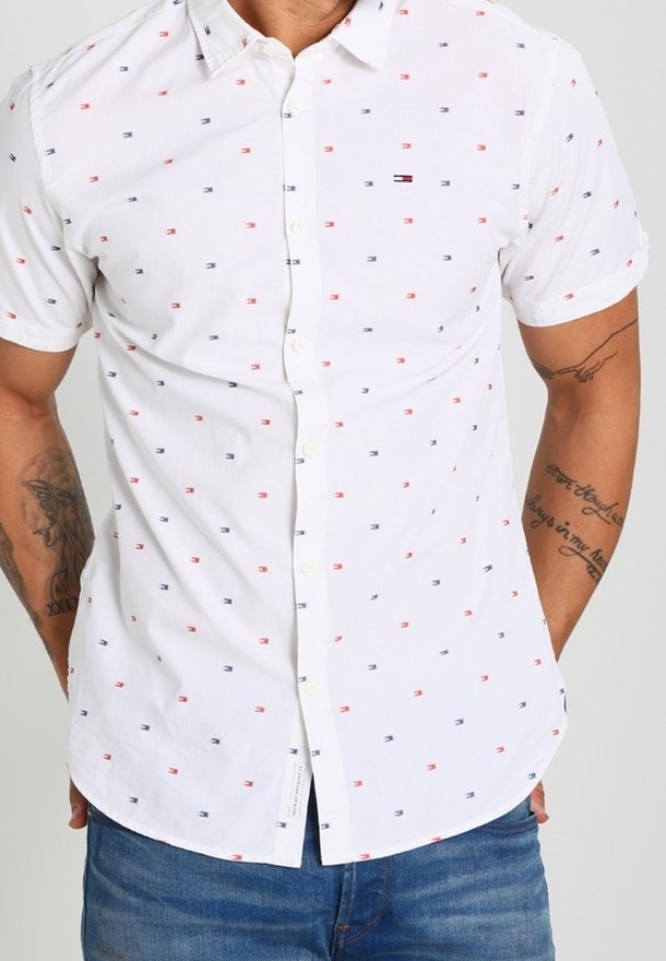 Camisa blanca de manga corta hecha de una tela ligera con pequeños patrones en azul y rojo y una tapeta de botones en la parte delantera.