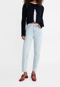 Marinblå kabelstickad kofta, vit kort topp, ljusblå högmidjade jeans och röda blockklackade skor med fyrkantig tå och remmar.