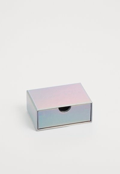 Rektangulær boks med iriserende overflade, metalliske kanter og et lille udskæring til åbning. Etiketten læser "MARIA BLACK" i prægede bogstaver.