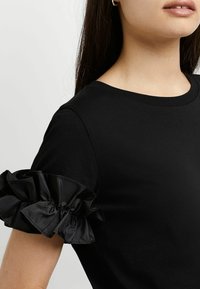 Camiseta negra de manga corta con acentos de satén rizado, textura suave y un clásico escote redondo.