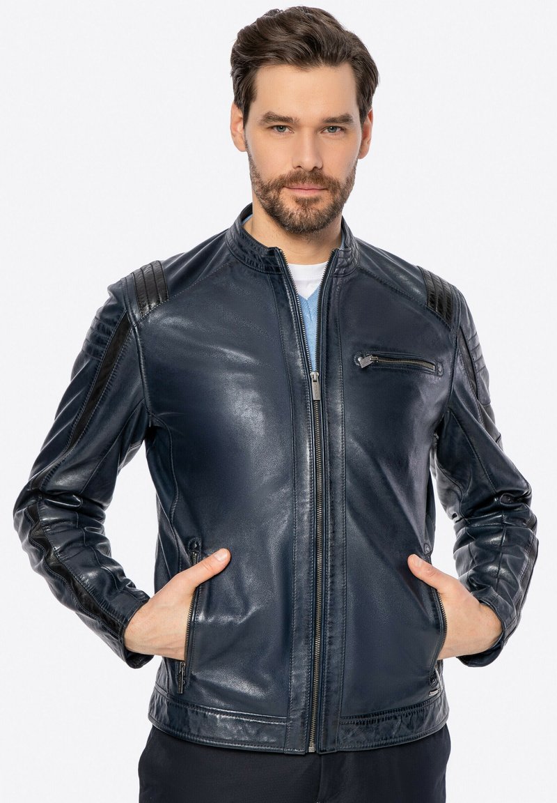 Giacca in pelle blu navy con chiusura a zip, dettagli trapuntati sulle spalle, tasca sul petto con zip, tasche laterali e texture liscia.