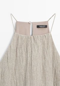 Beige gestructureerde mouwloze jurk met dunne bandjes, open rug met één knoop, label met de tekst "Massimo Dutti Made in China."