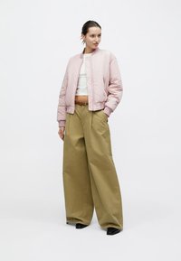 Giacca bomber rosa chiaro con polsini a costine, top bianco e pantaloni oversize color kaki. Scarpe nere con punta completano il look. Design semplice e moderno.