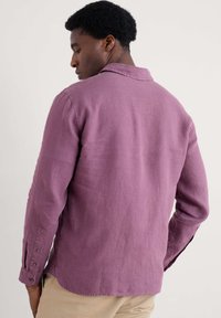 Camisa de manga larga de color púrpura claro con un cuello relajado, puños abotonados y un tejido texturizado, que presenta un dobladillo recto y un detalle en el yugo trasero.