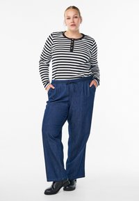 Svart och vit randig långärmad topp med knäppning i halsen, kombinerad med lösa blå jeans och svarta skor.
