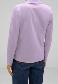 Fialový dlouhý rukáv s límečkem, hladká textura a rovný střih, ve spojení s tmavě modrými džíny s prošívanými kapsami.