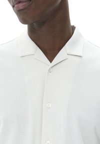 Witte polo met een zachte textuur, voorzien van een opstaande kraag, een sluiting met twee knopen en een schoon, minimalistisch ontwerp.