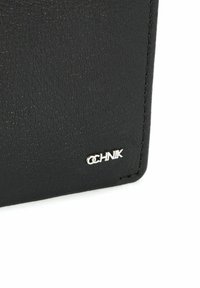 Czarny skórzany portfel o fakturowanej powierzchni z metalowym logo w kolorze srebrnym. Krawędzie są przeszywane, co podkreśla trwałość oraz detale projektu.