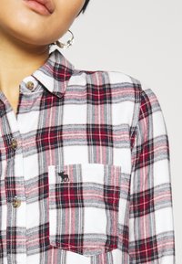 Camicia a quadri con bottoni, caratterizzata da un motivo a check bianco, rosso e grigio, con taschino sul petto e piccolo logo sul lato sinistro.