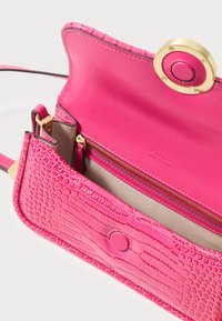 Bolsa de couro rosa com textura de crocodilo, apresentando um fecho de botão circular dourado e um bolso interior com fecho. Detalhe de costura intrincada.