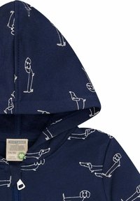 Giacca a vento blu navy con cappuccio realizzata in tessuto morbido, caratterizzata da illustrazioni di cani bianchi in varie pose. Include una cerniera frontale e un'etichetta visibile all'interno.