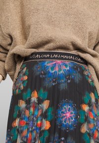 Bruine gebreide trui gecombineerd met een donkere geplooide rok met een levendige bloemenprint in blauw, groen, oranje en roze, met een versierde tailleband.