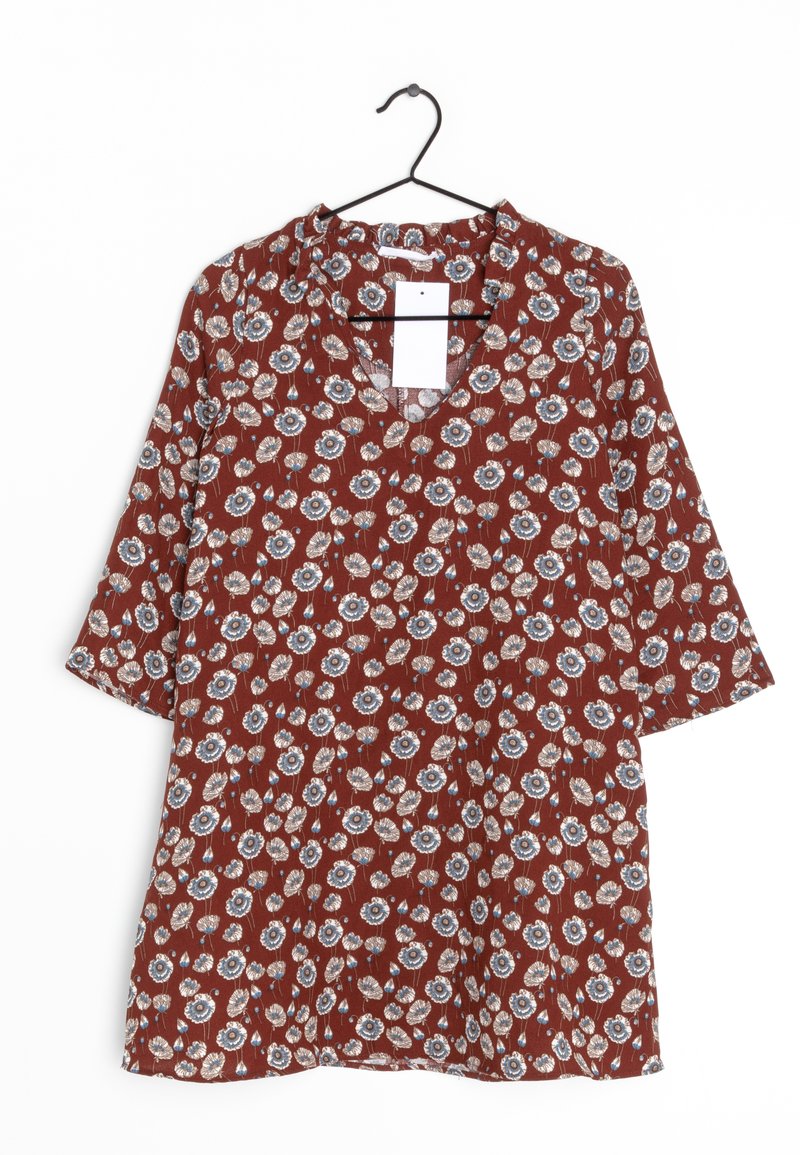 Rød blomsterkat med V-hals, trekvartlange ærmer, prydet med blå og hvide blomster mønstre på et tekstureret stof, hængende på en sort krog.