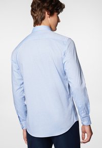 Jasnoniebieska koszula z długim rękawem w mały, ciemnoniebieski wzór w kratkę. Posiada standardowy kołnierzyk oraz mankiety na jeden guzik. Gładka struktura materiału.