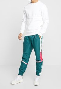 Sudadera blanca con cuello redondo, combinada con pantalones jogger en teal con acentos en rosa y crema. Llevado con zapatillas blancas.