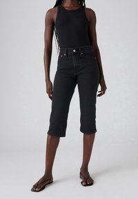 Jeans cortos de mezclilla negros con cintura alta, con cierre de botón y cinco bolsillos, combinados con una camiseta sin mangas negra de canalé.