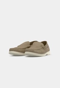 Beige suede slip-on shoes with white rubber sole, rounded toe, and stitched detailing on the upper. Minimalistic design without visible hardware.
