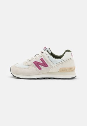 Zapatilla New Balance en beige y blanco con el logo "N" rosa, forro interior verde y suela beige con dibujo negro sobre fondo blanco.