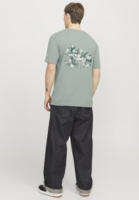 Lichtgroene katoenen t-shirt met een bloemen- en logo-afbeelding op de achterkant, gecombineerd met donkerblauwe denim broeken met opgerolde pijpen.