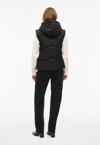 Juoda pūsta liemenė su gobtuvu, siuvinėtomis dalimis ir aukšta apykakle. Derinama su kreminėmis rankovėmis, juodomis korduro kelnėmis ir aulinukais su kulnais.