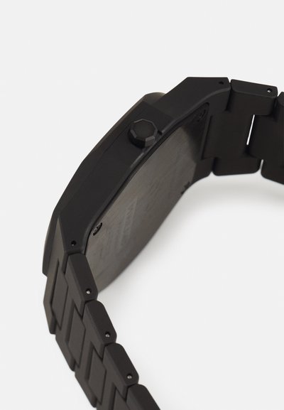 Μαύρο ρολόι χεριού με οκταγωνιαία θήκη, υφασμένα λουριά και έντονο εξαγωνικό κορώνα. Διαθέτει ματ φινίρισμα και τετράγωνα σκηνάκια.