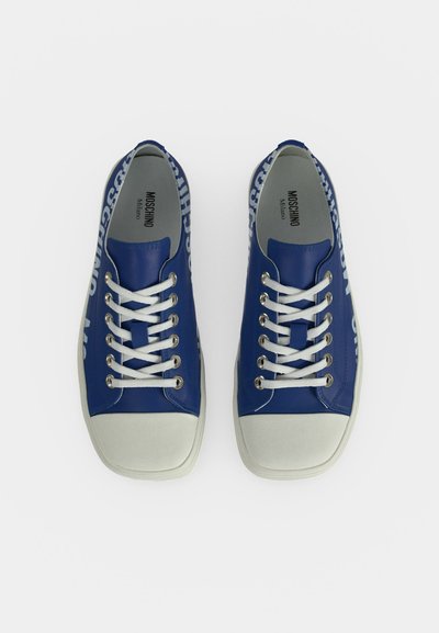 Paire de baskets Moschino bleues avec des lacets blancs, des bouts blancs et un marquage blanc le long des côtés, vues de dessus sur fond blanc.